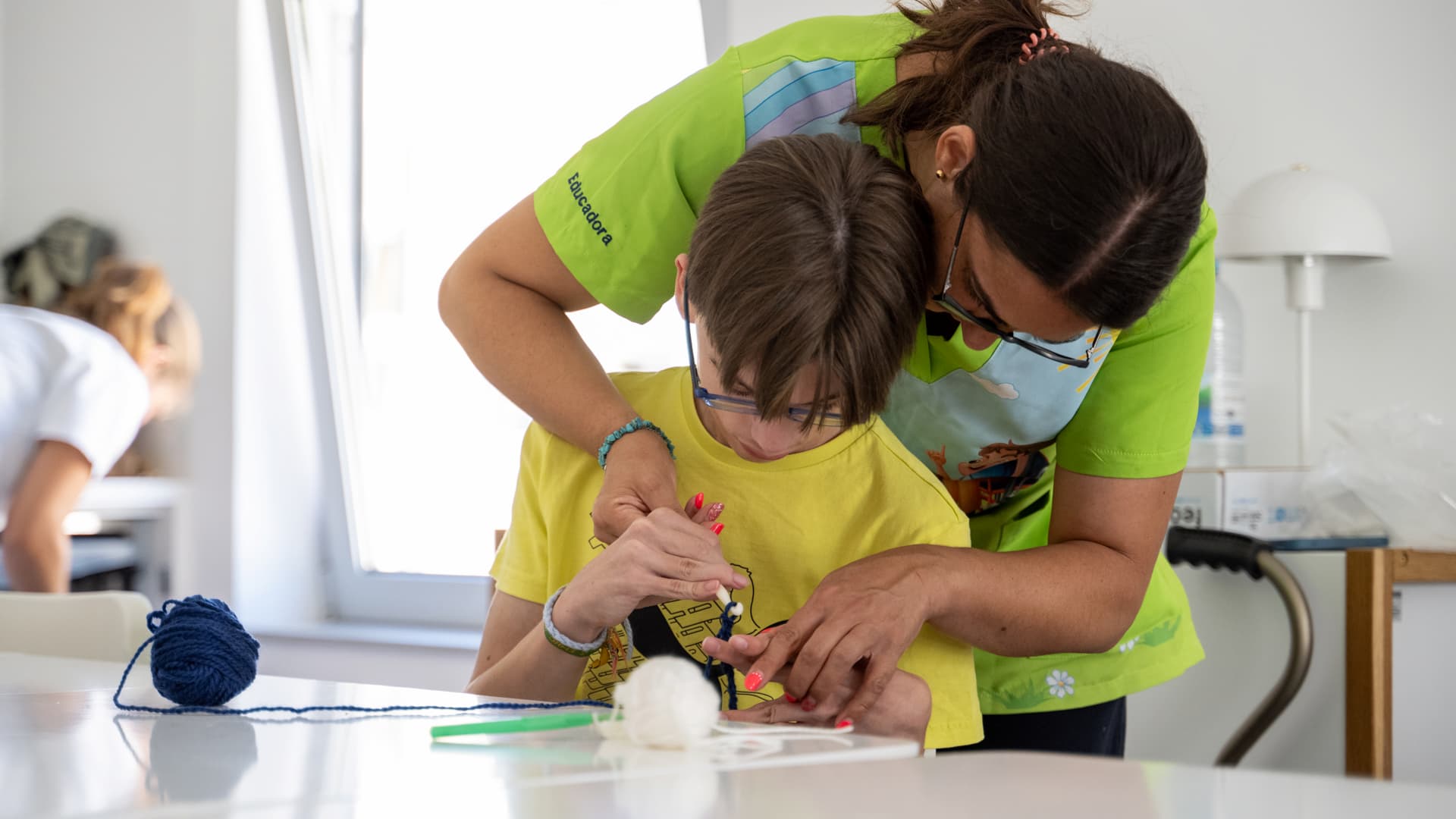 Uma cuidadora ajuda um menino a trabalhar com lã para artesanato