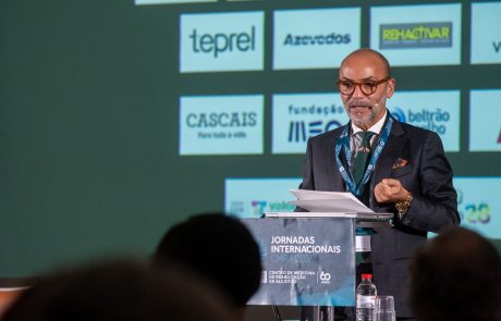 Orador de fato escuro e gravata verde intervém ao púlpito nas Jornadas Internacionais de Reabilitação CMRA 2026, perante um ecrã com os logótipos dos patrocinadores.